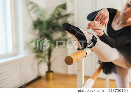 Young ballerina in tutu skirt stretching practicing ballet positions dancing near ballet barre in dance class. Young classical dancer woman in dance studio. Ballet class training Ballet school concept Young ballerina in tutu skirt stretching practicing ballet positions dancing near ballet barre in dance class. Young classical dancer woman in dance studio. Ballet class training Ballet school concept 138730164