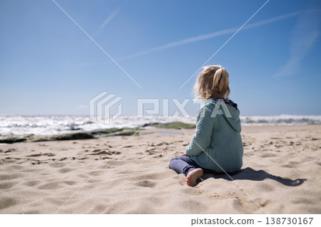 Little 4-year-old girl relaxing on a quiet beach during springtime Little 4-year-old girl relaxing on a quiet beach during springtime 138730167