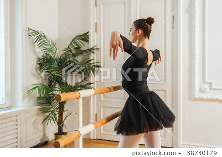 Young ballerina in tutu skirt stretching practicing ballet positions dancing near ballet barre in dance class. Young classical dancer woman in dance studio. Ballet class training Ballet school concept Young ballerina in tutu skirt stretching practicing ballet positions dancing near ballet barre in dance class. Young classical dancer woman in dance studio. Ballet class training Ballet school concept 138730179
