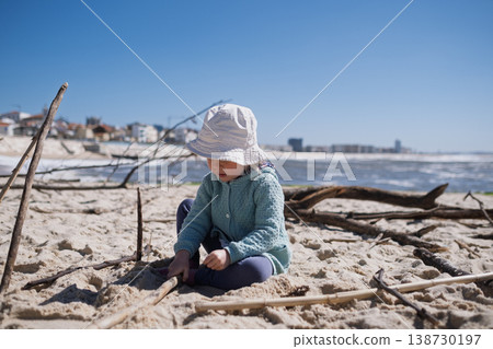 Little 4 year old girl playing with wooden sticks on a sandy beach Little 4 year old girl playing with wooden sticks on a sandy beach 138730197