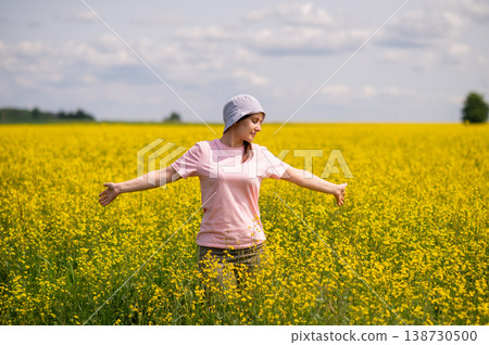 Woman in a bucket hat stands in yellow rapeseed field, enjoying the warmth and peace of a sunny summer day Woman in a bucket hat stands in yellow rapeseed field, enjoying the warmth and peace of a sunny summer day 138730500