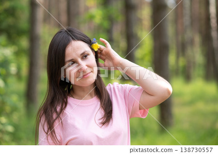 Woman placing a yellow flower behind her ear in a sunny forest, enjoying peaceful moment in nature Woman placing a yellow flower behind her ear in a sunny forest, enjoying peaceful moment in nature 138730557