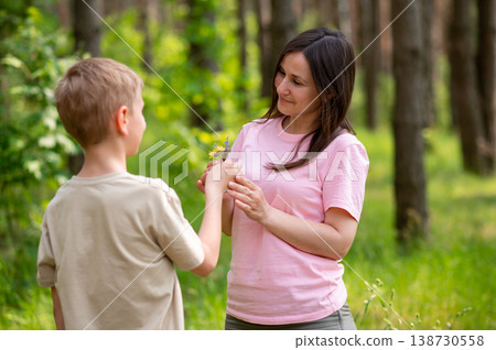 Boy giving a flower to his mother in a sunny forest clearing, tender family moment in nature Boy giving a flower to his mother in a sunny forest clearing, tender family moment in nature 138730558