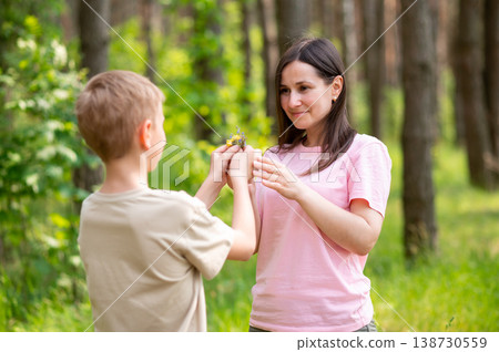 Boy giving a flower to his mother in a sunny forest clearing, tender family moment in nature Boy giving a flower to his mother in a sunny forest clearing, tender family moment in nature 138730559