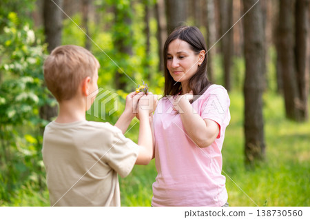 Boy giving a flower to his mother in a sunny forest clearing, tender family moment in nature Boy giving a flower to his mother in a sunny forest clearing, tender family moment in nature 138730560