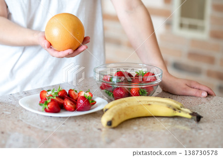 woman's hand holding grapefruit, banana and strawberry on table, preparing for breakfast woman's hand holding grapefruit, banana and strawberry on table, preparing for breakfast 138730578