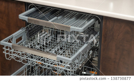Close-up of open dishwasher with top and bottom racks pulled out displaying interior structure. Kitchen appliance detail, dishwasher racks, home equipment view, cleaning setup. Close-up of open dishwasher with top and bottom racks pulled out displaying interior structure. Kitchen appliance detail, dishwasher racks, home equipment view, cleaning setup. 138730877