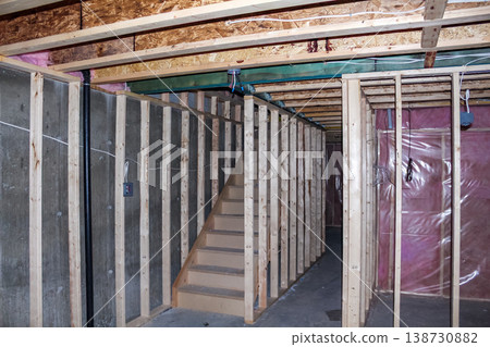 Interior view of an unfinished basement construction site featuring wooden framing, exposed walls, and a staircase leading to the upper level Interior view of an unfinished basement construction site featuring wooden framing, exposed walls, and a staircase leading to the upper level 138730882