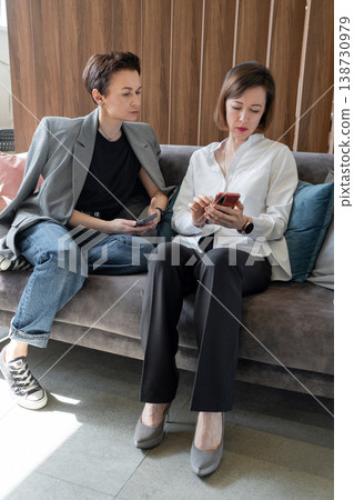 Women working closely and pointing at screen of smartphone while sitting on sofa in office. Communication, smartphone, teamwork, office, businesswomen. Women working closely and pointing at screen of smartphone while sitting on sofa in office. Communication, smartphone, teamwork, office, businesswomen. 138730979