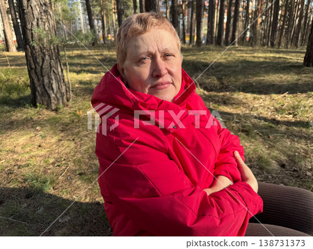 A woman sits in the forest on a stump in a red jacket on a sunny day among the trees A woman sits in the forest on a stump in a red jacket on a sunny day among the trees 138731373