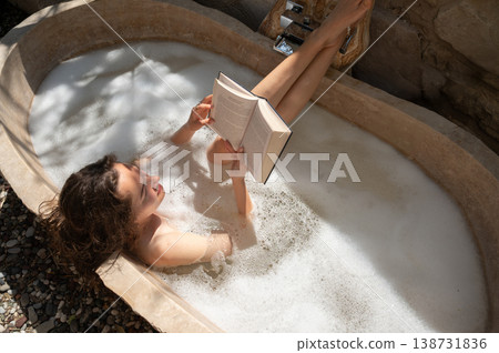 Young Woman Reading a Book While Taking a Relaxing Bubble Bath Outdoors Young Woman Reading a Book While Taking a Relaxing Bubble Bath Outdoors 138731836