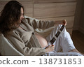 Pregnant woman looking at ultrasound scan while sitting on armchair 138731853