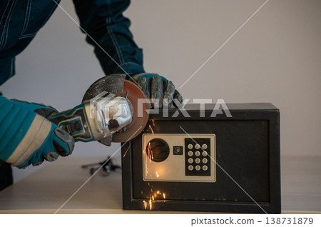 A man breaks into a safe with a grinder. A man breaks into a safe with a grinder. 138731879