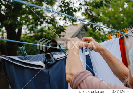 Woman attaches clothes with clothespins to ropes for drying outside Woman attaches clothes with clothespins to ropes for drying outside 138732604