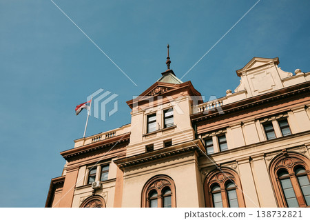 Elegant historic building with tower and Serbian flag against blue sky in Belgrade. Concept of heritage, identity and architecture. Elegant historic building with tower and Serbian flag against blue sky in Belgrade. Concept of heritage, identity and architecture. 138732821