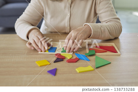 Cropped portrait of senior woman collecting wooden geometric figures at home sitting at the table 138733288