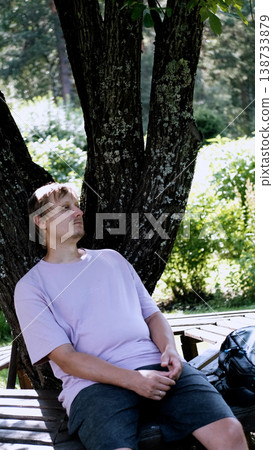 Relaxing man in a park on a bench in summer, enjoying the fresh air, vacation, or relaxing alone in the garden. A thoughtful, smiling, or calm man in nature, resting or waiting in a natural setting. Relaxing man in a park on a bench in summer, enjoying the fresh air, vacation, or relaxing alone in the garden. A thoughtful, smiling, or calm man in nature, resting or waiting in a natural setting. 138733879