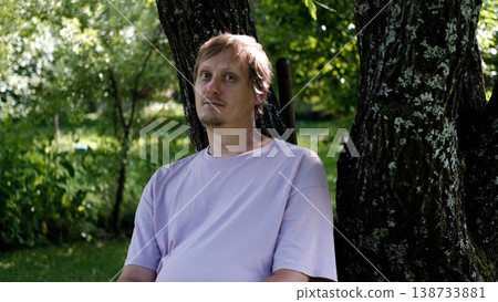 Relaxing man in a park on a bench in summer, enjoying the fresh air, vacation, or relaxing alone in the garden. A thoughtful, smiling, or calm man in nature, resting or waiting in a natural setting. 138733881