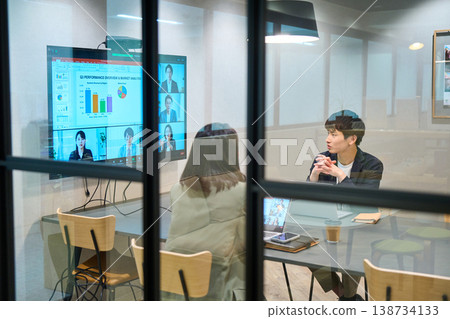 A man and woman from a foreign company conduct a web conference with their remote team in a glass-walled conference room. A man and woman from a foreign company conduct a web conference with their remote team in a glass-walled conference room. 138734133