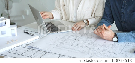Architects engaging in a professional meeting, reviewing detailed blueprints on a table, utilizing a laptop, and collaborating on building design and construction planning Architects engaging in a professional meeting, reviewing detailed blueprints on a table, utilizing a laptop, and collaborating on building design and construction planning 138734518