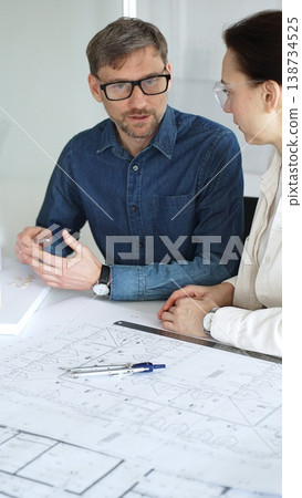 Architects collaborating on blueprint plans, discussing engineering details and project designs, planning construction development with a laptop in a modern office environment 138734525