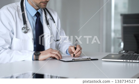 Adult male doctor writing medical prescription paperwork in clinic office, healthcare professional filling patient form. Medicine, healthcare and science concept Adult male doctor writing medical prescription paperwork in clinic office, healthcare professional filling patient form. Medicine, healthcare and science concept 138734527