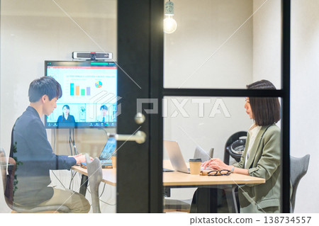 一名男子和一名女子在玻璃牆會議室與遠端團隊進行網路會議。 一名男子和一名女子在玻璃牆會議室與遠端團隊進行網路會議。 138734557