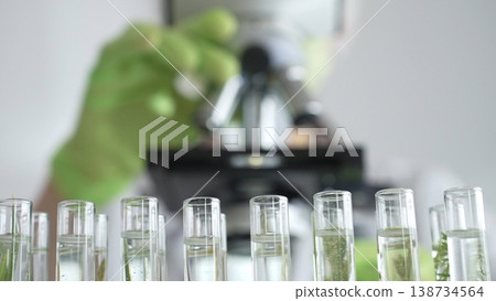Close up of test tubes with a scientist analyzing plant samples in test tubes with a microscope, conducting research in a laboratory. Medicine, healthcare and science concept Close up of test tubes with a scientist analyzing plant samples in test tubes with a microscope, conducting research in a laboratory. Medicine, healthcare and science concept 138734564