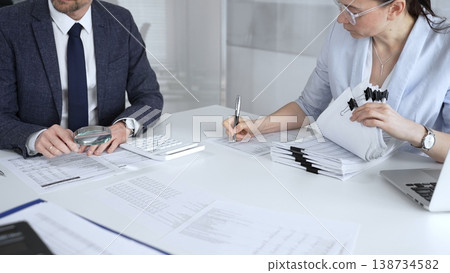 Professional auditors reviewing financial paperwork, using magnifying glass and calculator while analyzing business documents for detailed inspection and accounting compliance. Audit and taxes 138734582