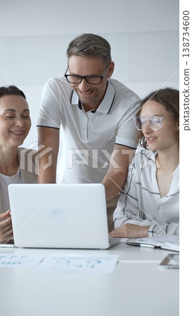 Business people team collaborating and analyzing data on a laptop during an office meeting, uniting efforts to reach shared objectives and drive successful outcomes together 138734600