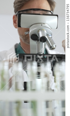 Scientific researcher in protective gear analyzing specimens through a microscope in a sterile laboratory environment. Medicine, healthcare and science concept 138734795