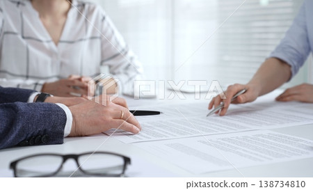 Business people discussing contract details during an important corporate meeting, partners reviewing legal documents with an attorney, collaborating on an agreement Business people discussing contract details during an important corporate meeting, partners reviewing legal documents with an attorney, collaborating on an agreement 138734810