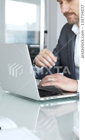 Professional hand typing on laptop keyboard at glossy desk with eyeglasses nearby and blurred financial documents, conveying modern office work, data analysis and business communication 138734837