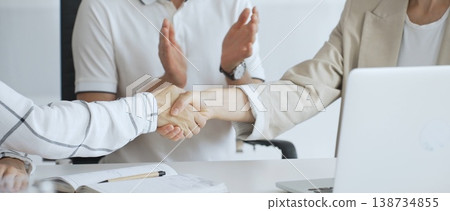 Businesswomen shaking hands after successful negotiation, colleagues clapping, celebrating agreement or partnership in modern office, laptop and documents on table, close up 138734855