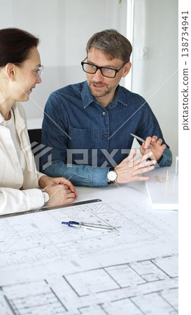 Architects collaborating on blueprint plans, discussing engineering details and project designs, planning construction development with a laptop in a modern office environment Architects collaborating on blueprint plans, discussing engineering details and project designs, planning construction development with a laptop in a modern office environment 138734941