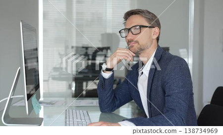 Professional businessman in a blue jacket working on desktop computer in modern office, focusing on his work and business tasks. Business people concept Professional businessman in a blue jacket working on desktop computer in modern office, focusing on his work and business tasks. Business people concept 138734969
