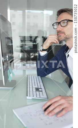 Businessman in a blue jacket thinking and brainstorming ideas while working on computer and taking notes in modern office. Business people concept Businessman in a blue jacket thinking and brainstorming ideas while working on computer and taking notes in modern office. Business people concept 138735012