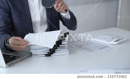 Auditor or accountant inspecting financial documents with a magnifying glass. Analyzing corporate tax records. Legal data. Invoice details. Or business reports. Audit and taxes 138735062