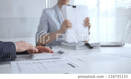 Business professionals working on financial reports, calculating taxes and managing paperwork at an office desk, collaborating on accounting tasks and corporate documentation. Audit and taxes 138735135