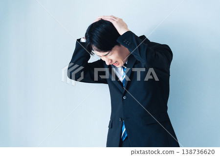 A young man in a suit holding his head in his hands. 138736620