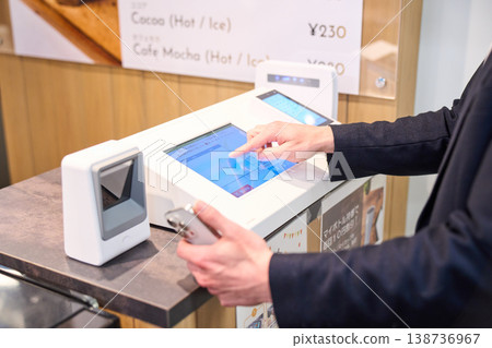 一家外國公司的軟體工程師用他的智慧型手機在公司咖啡廳的自助結帳櫃檯付款。 一家外國公司的軟體工程師用他的智慧型手機在公司咖啡廳的自助結帳櫃檯付款。 138736967