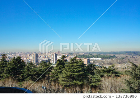 A view of the city unfolding under a blue sky, seen through the trees from a hilltop on the outskirts of Madrid. A view of the city unfolding under a blue sky, seen through the trees from a hilltop on the outskirts of Madrid. 138736990