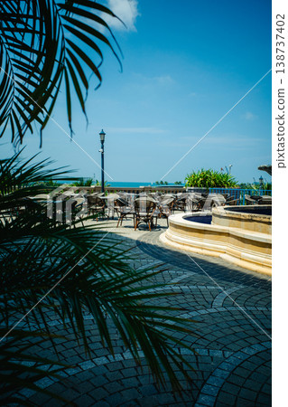 A view of a seaside terrace with a fountain, seen through palm leaves. A view of a seaside terrace with a fountain, seen through palm leaves. 138737402