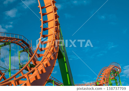 Abstract detail of empty orange roller coaster loops against a bright blue sky Abstract detail of empty orange roller coaster loops against a bright blue sky 138737709