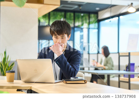 一位年輕男子在公司開放式辦公室使用筆記型電腦工作。 138737908