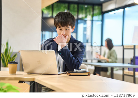 A young man working on his laptop in a company's open office. A young man working on his laptop in a company's open office. 138737909