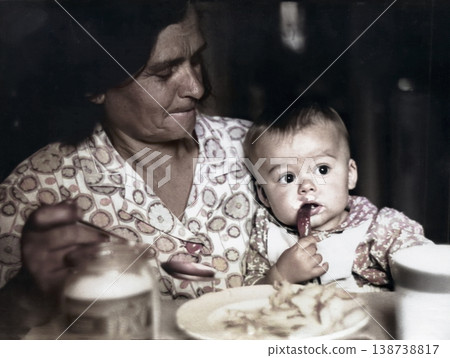 A vintage portrait of a grandmother and her young grandson. The grandmother teaches the child to eat from a plate with a spoon. Retro photo from 1968. A vintage portrait of a grandmother and her young grandson. The grandmother teaches the child to eat from a plate with a spoon. Retro photo from 1968. 138738817