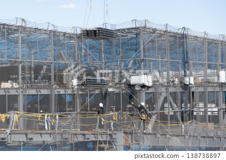 三名工人引導起重機吊起的地板材料，然後將其放到建築工地的地面上。 138738897