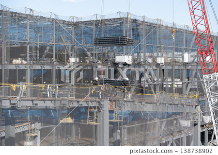 Eight workers guide flooring materials that have been lifted by a crane and then lower them to the ground at a construction site. 138738902