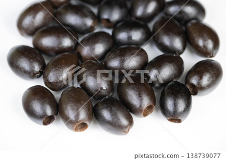 Scattered black olives on white surface with soft shadows and varied sizes, casual pantry vibe evokes Mediterranean flavor, ideal for recipe, snack, or ingredient lifestyle imagery 138739077